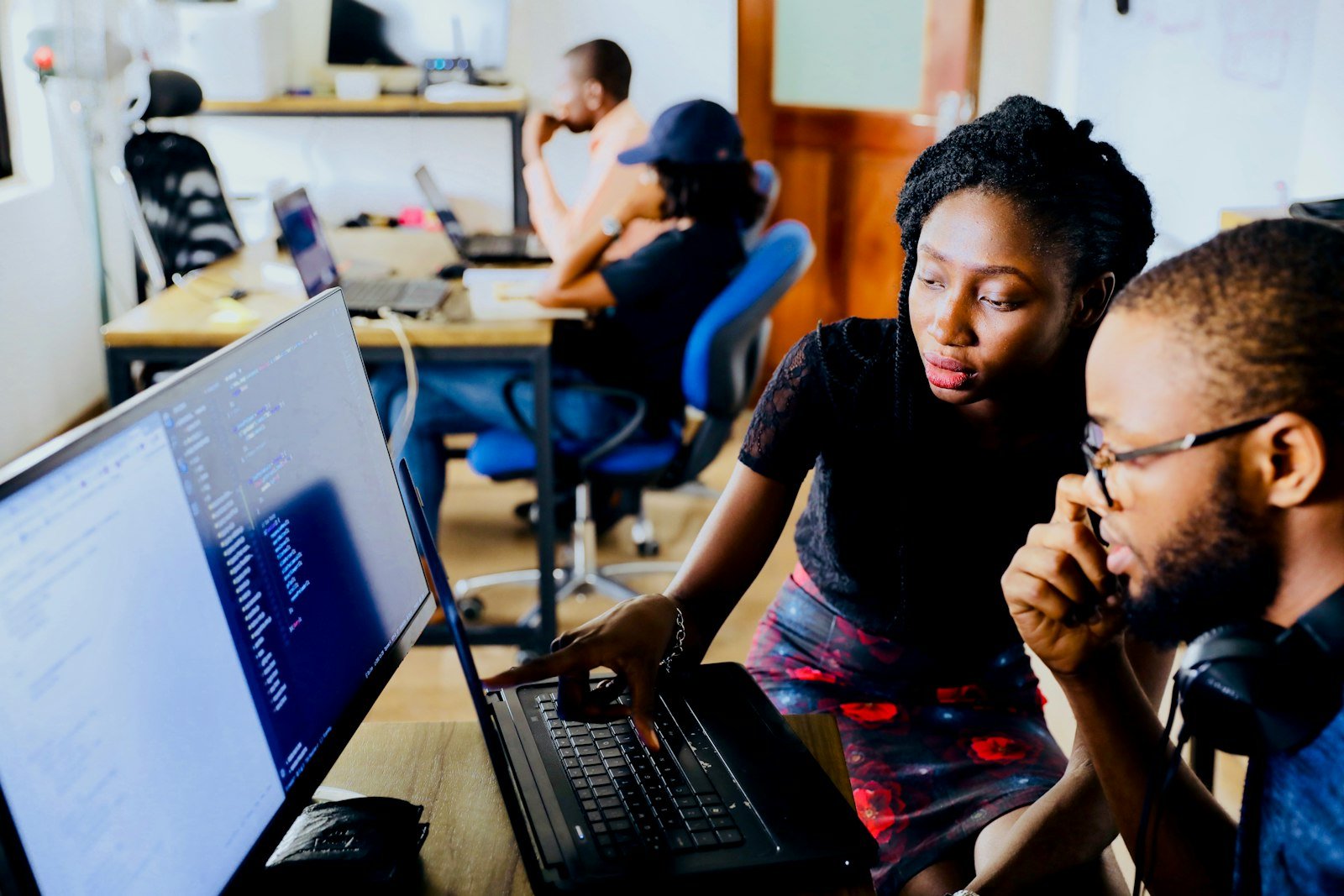 Two SF Fellows working through code together at a shared workstation in a real office